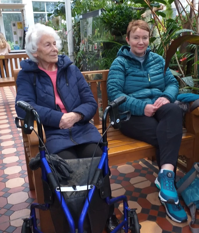 Two women sitting on a bench, one with a walking frame